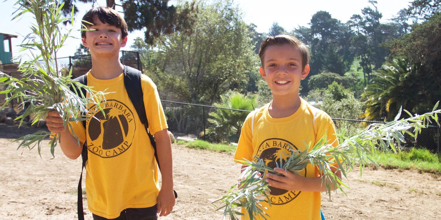 two boys holding plants and wearing Zoo Camp shirts